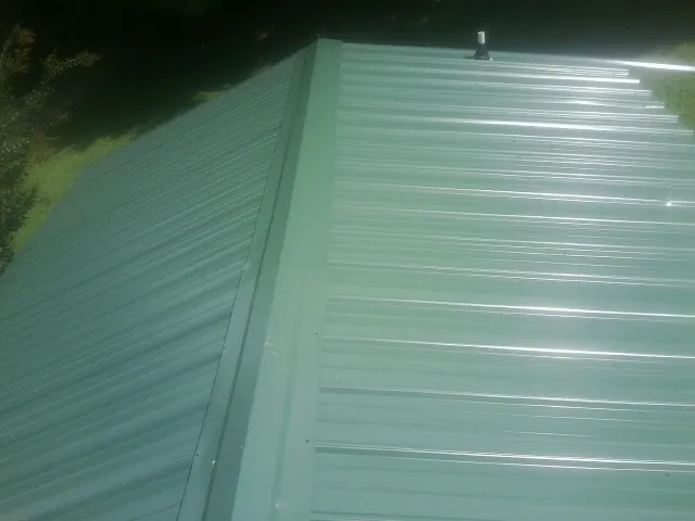 New green metal panels meeting at the ridge of a roof — Flat Roof Repair work by our crew in Boynton Beach