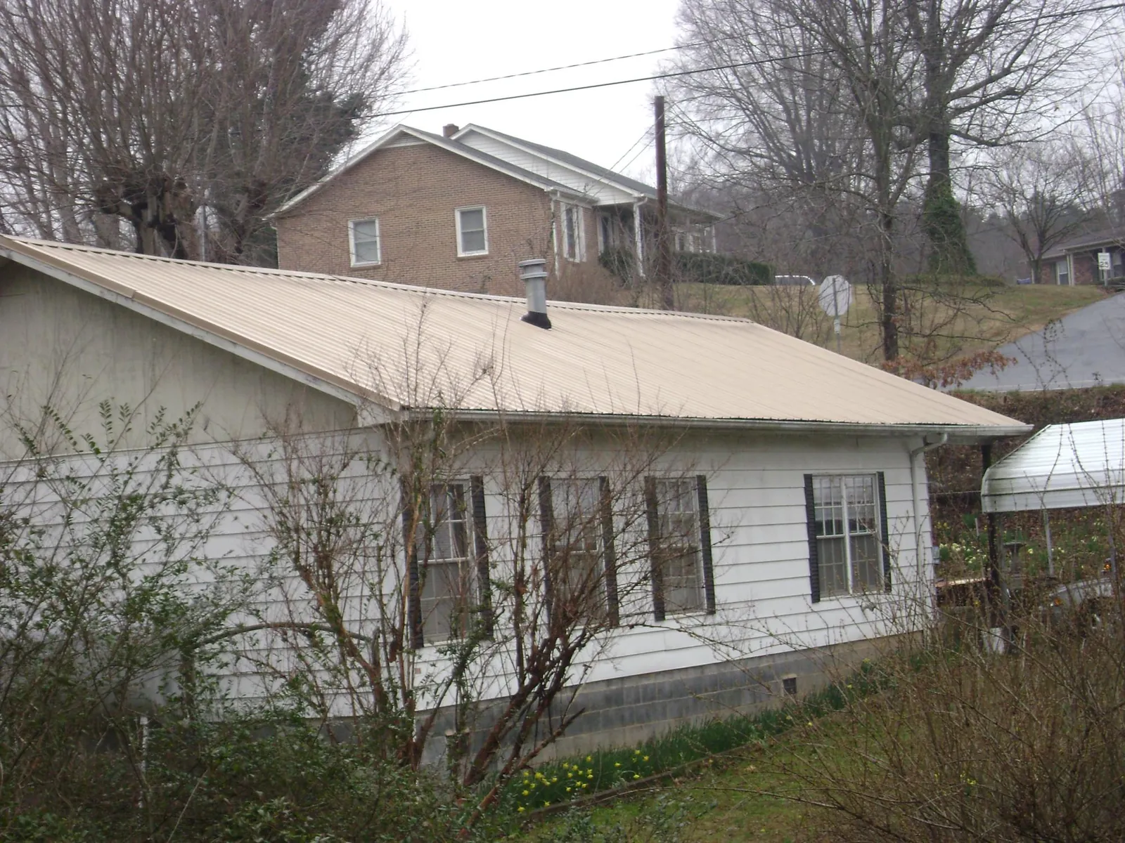 Tan metal roof on a white sided house set into a hillside — Commercial Roofing by Roofing Brothers in Boynton Beach